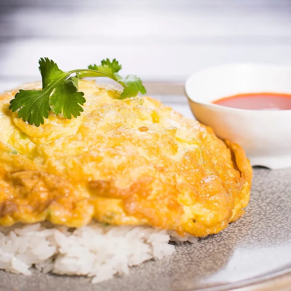 Golden Thai omelet with cilantro on white rice, served with a side of red chili sauce.