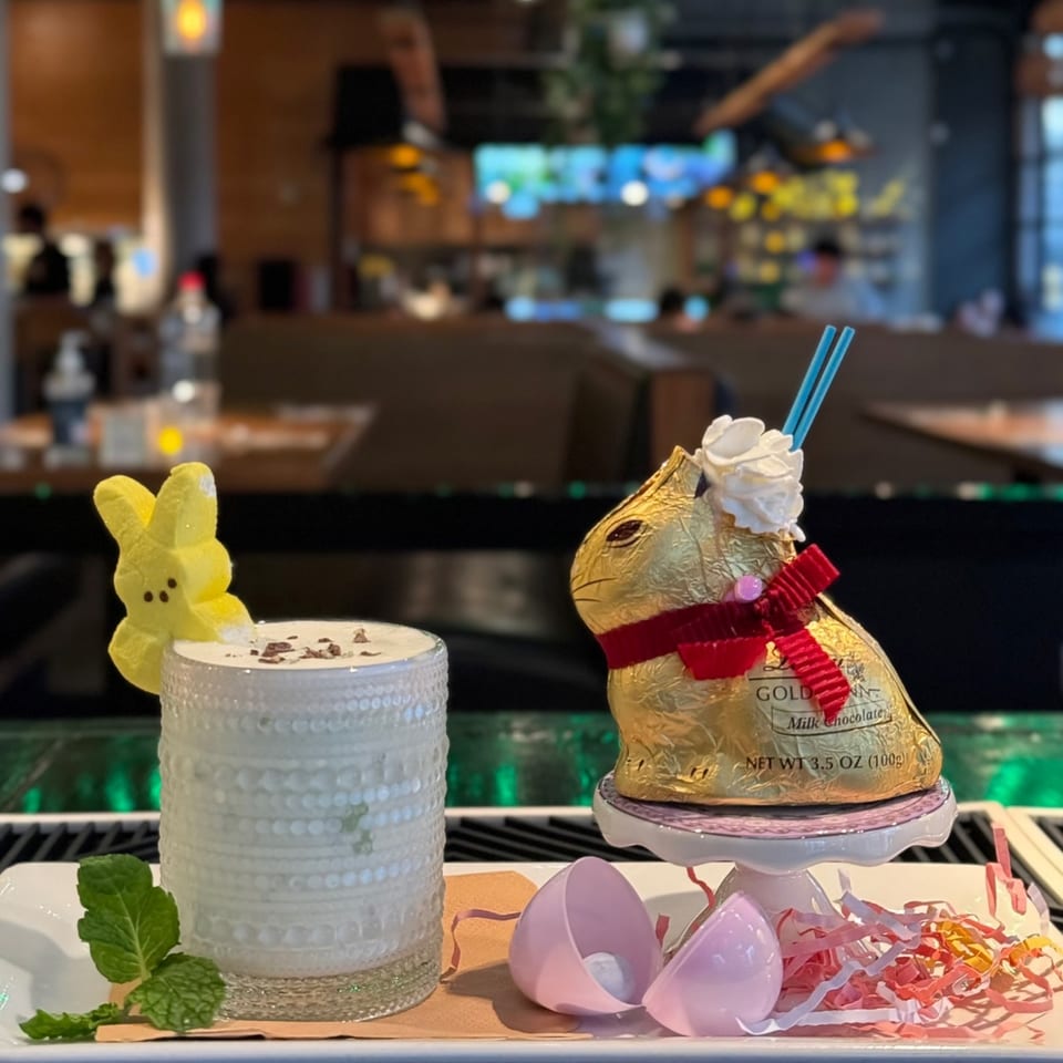 A festive Easter-themed drink with a Peep, chocolate bunny, and plastic eggs on a bar.