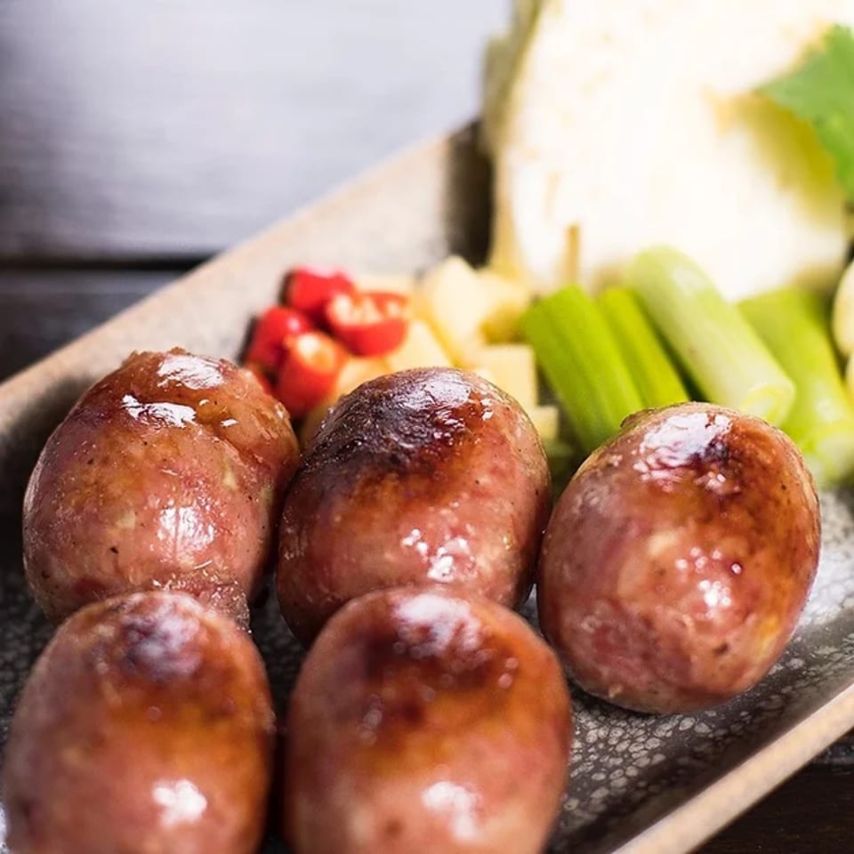 Close-up of five grilled Thai sausages with fresh cabbage, chilies, and ginger on a plate.