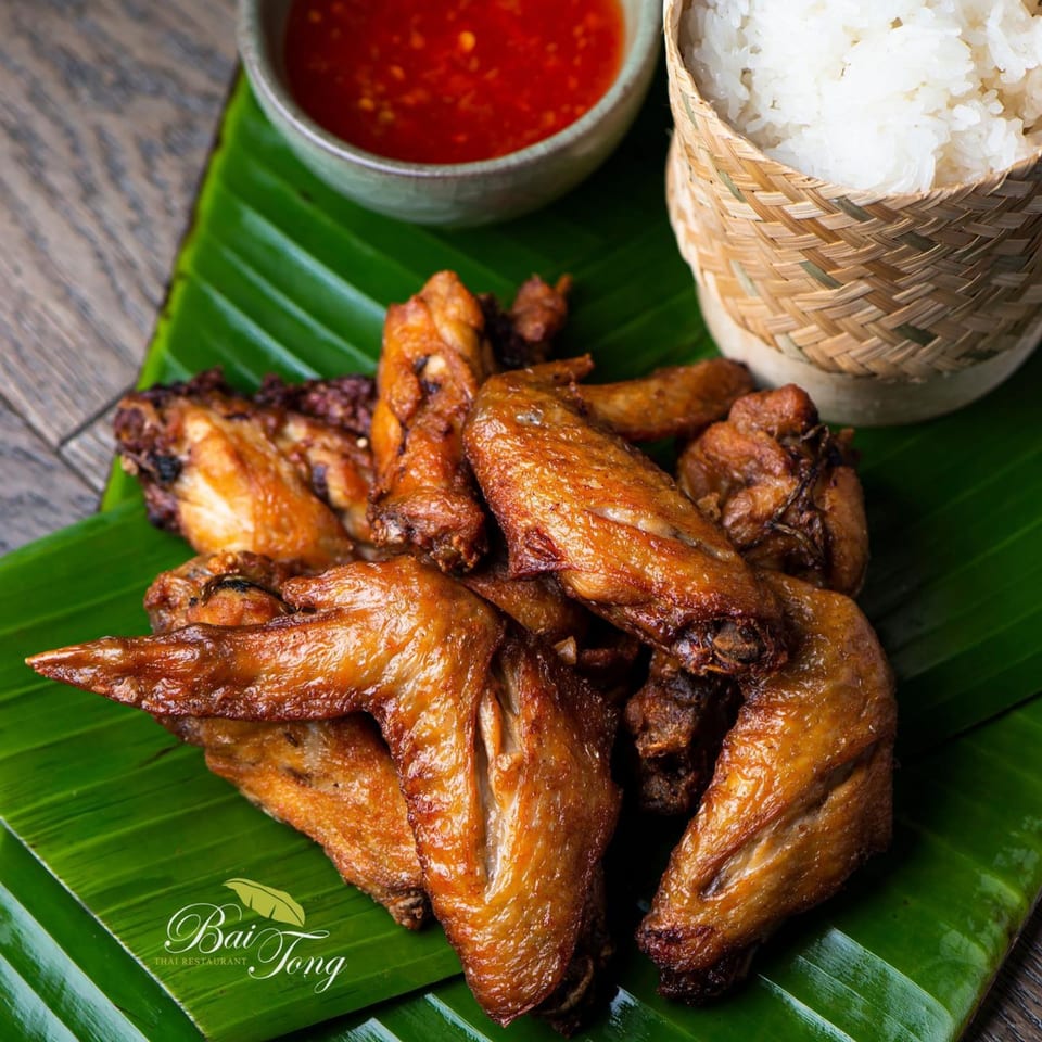 Crispy fried chicken wings on a banana leaf, with sticky rice and chili sauce.