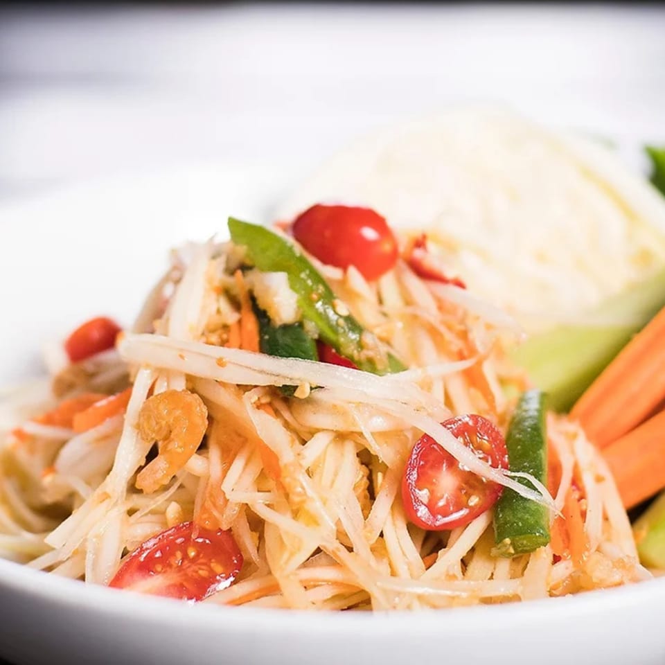 Close-up of a Thai papaya salad with cherry tomatoes, green beans, and dried shrimp.